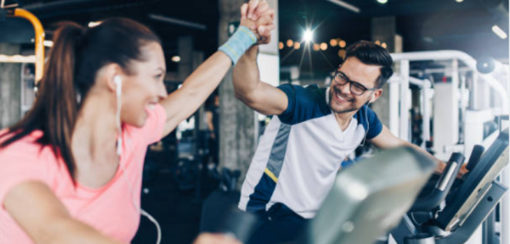 A man and a women on exercise bikes giving each other a high five